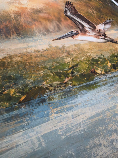 Pelican flying over a coastal landscape with water and sand.