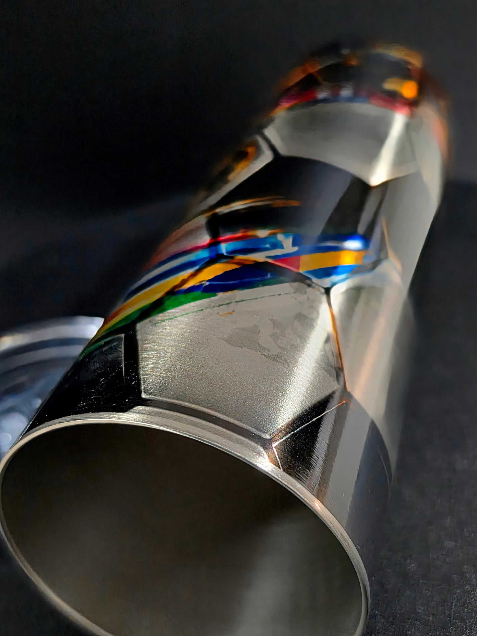 Close-up of a metallic exhaust tip with colorful stripes on a dark background