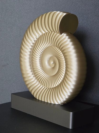 A large decorative ammonite shell sculpture in a warm cream-beige tone, displayed upright on a dark rectangular pedestal against a dark gray wall.